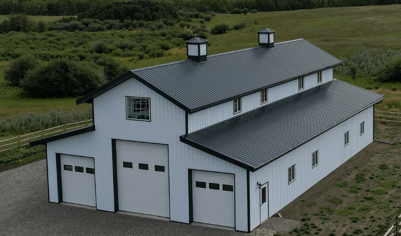 A bright white post-frame equestrian barn with two overhead doors and two cupolas