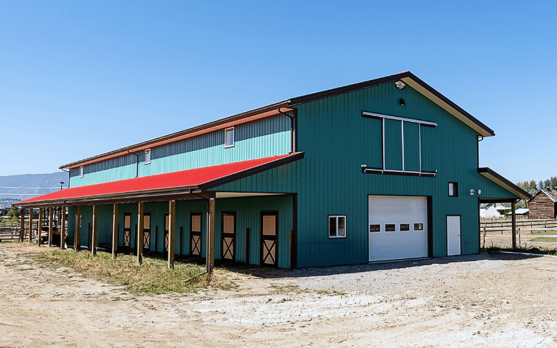 A turquoise post-frame equestrian barn with two overhead doors, and sliding doors