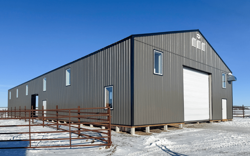 A charcoal post-frame equestrian barn with four overhead doors