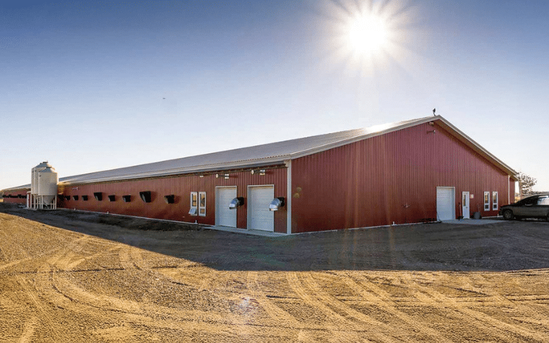 A dark red post-frame equestrian barn with four overhead and four bi-fold doors