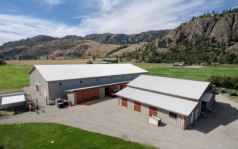 A stone grey post-frame riding arena with soffits, sliding doors, and overhead doors