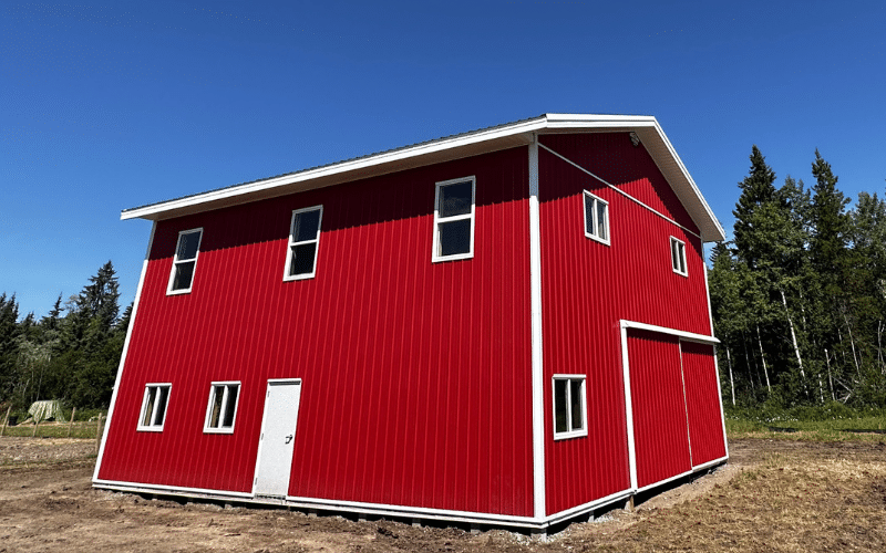 A bright red post-frame equestrian barn with sliding doors