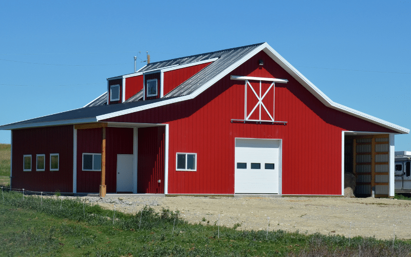 A bright red equestrian post-frame barn with an overhead door