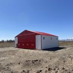 A bright white post-frame airplane hangar with a bright red bi-fold door and roof
