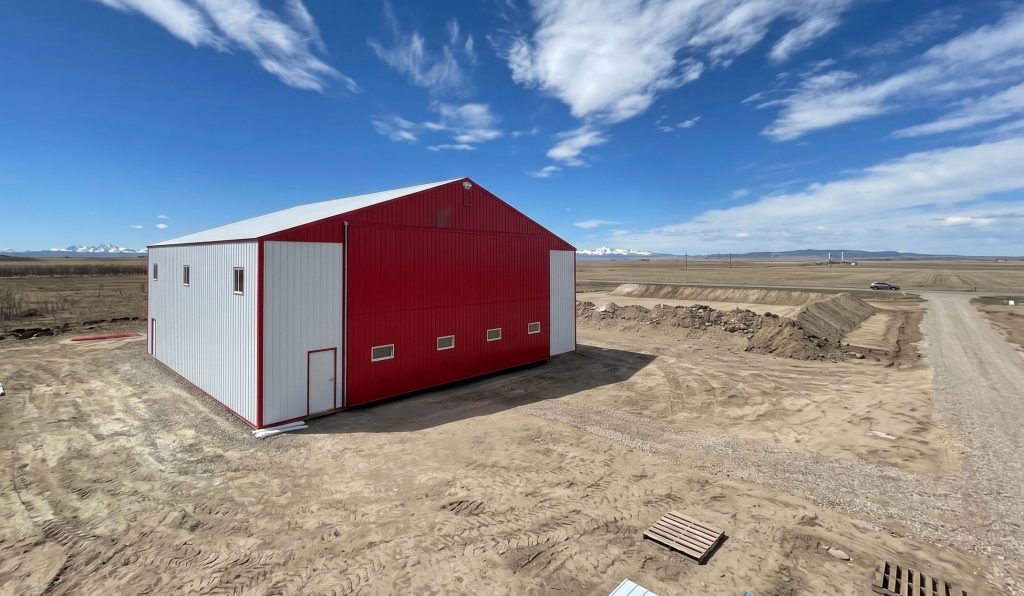 A bright white post-frame airplane hangar with a bright red bi-fold door and roof