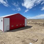 A bright white post-frame airplane hangar with a bright red bi-fold door and roof
