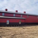 A dark red agricultural post-frame shop with two overhead doors, timber accents, crows peak, and a bi-fold door