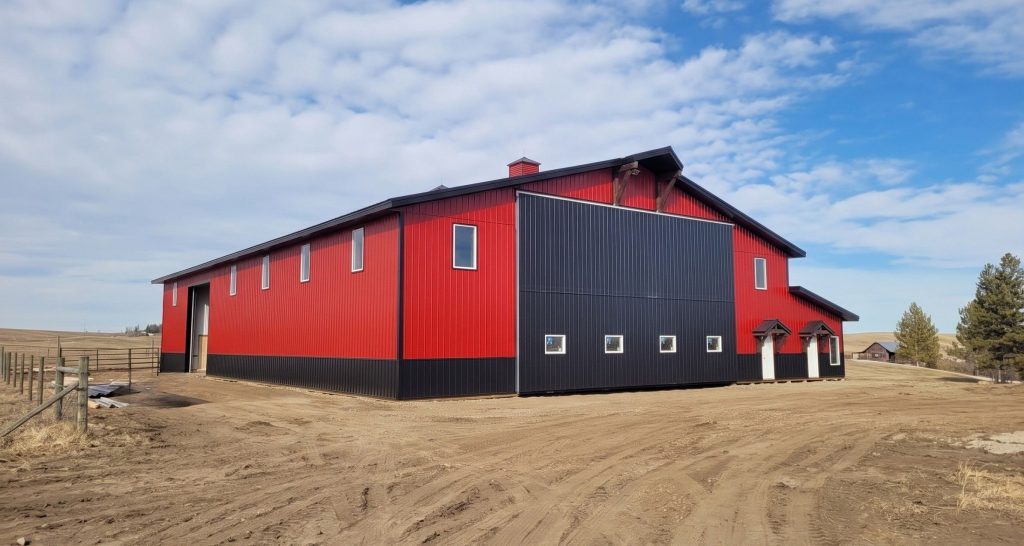 A dark red agricultural post-frame shop with two overhead doors, timber accents, crows peak, and a bi-fold door