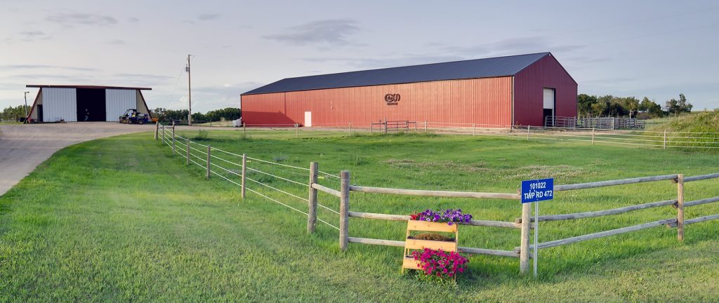 A dark red post-frame riding arena with a chain overhead door
