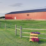 A dark red post-frame riding arena with a chain overhead door