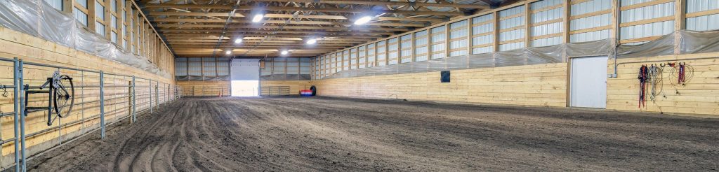 A dark red post-frame riding arena with a chain overhead door