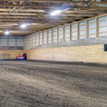 A dark red post-frame riding arena with a chain overhead door