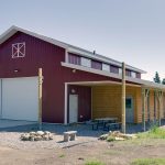 A dark red post-frame equestrian barn