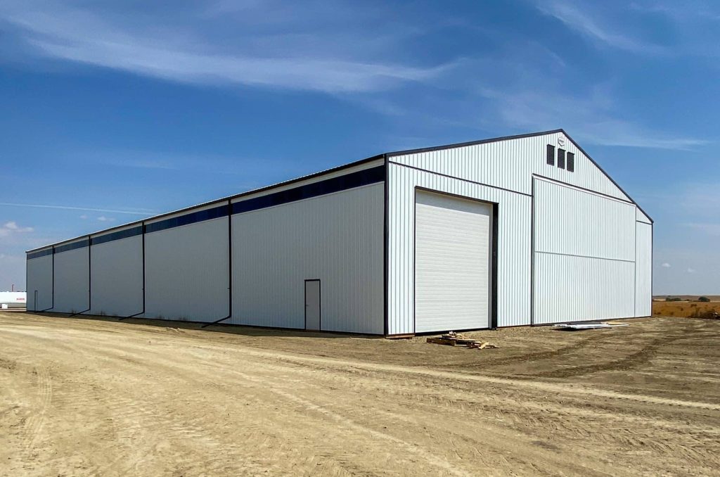 A bright white post-frame agricultural storage building with bi-fold and overhead doors