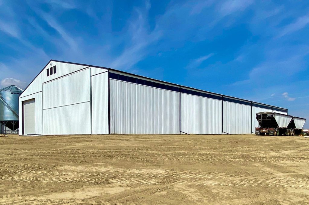 A bright white post-frame agricultural storage building with bi-fold and overhead doors