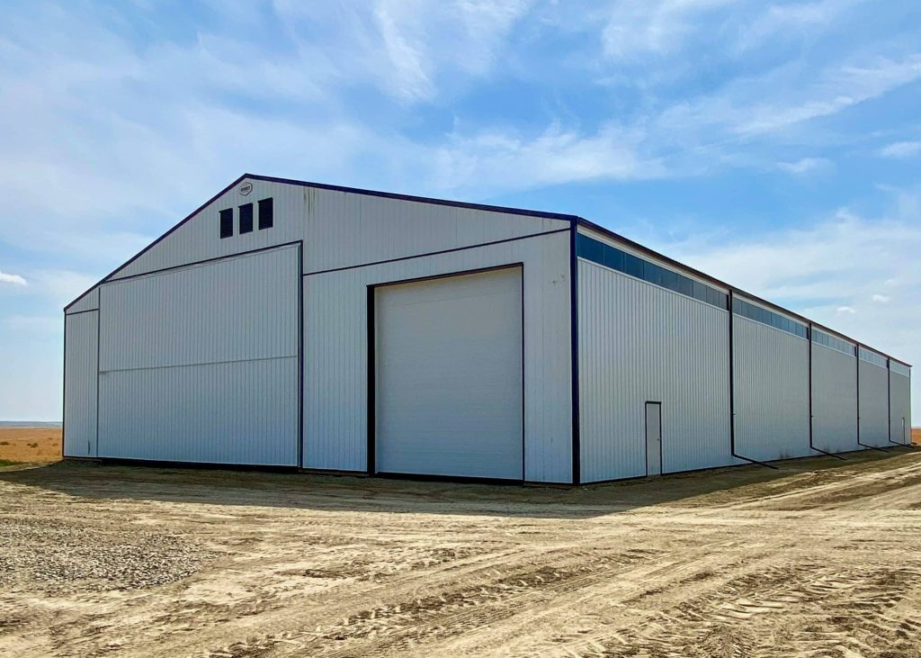A bright white post-frame agricultural storage building with bi-fold and overhead doors