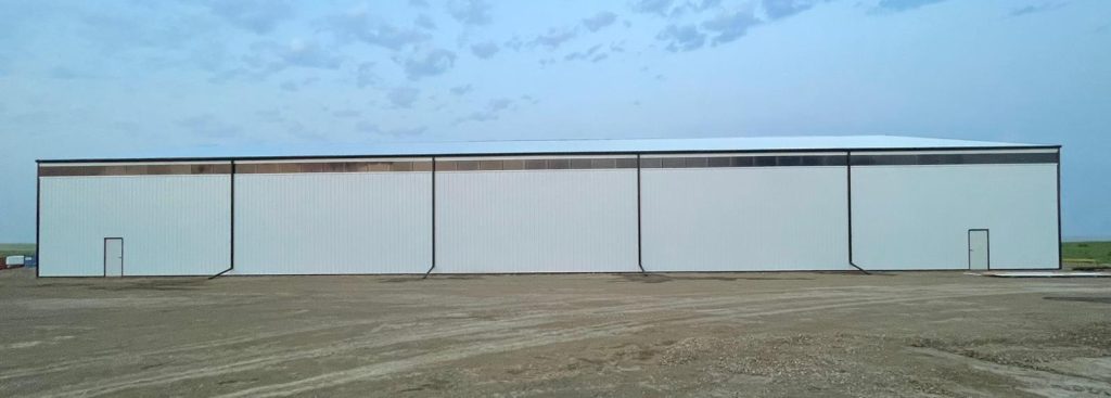 A bright white post-frame agricultural storage building with bi-fold and overhead doors