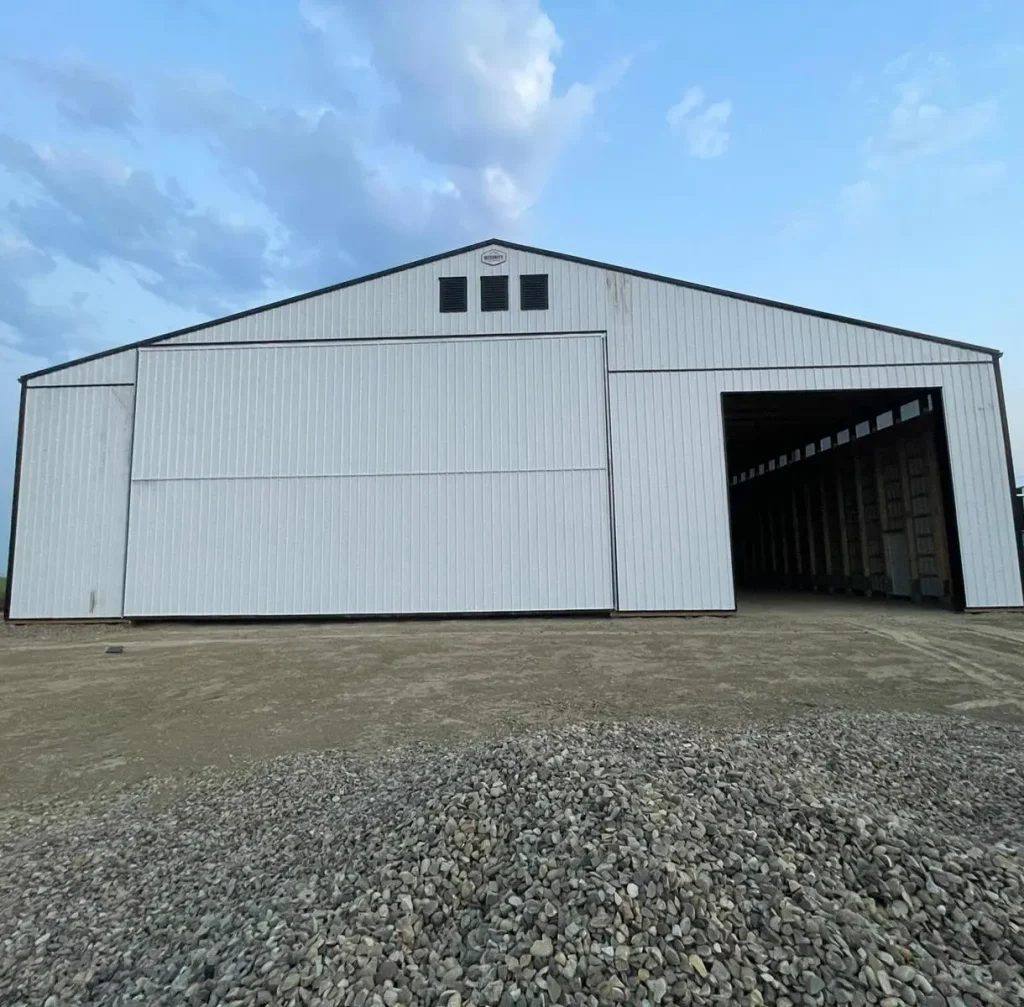 A bright white post-frame agricultural storage building with bi-fold and overhead doors
