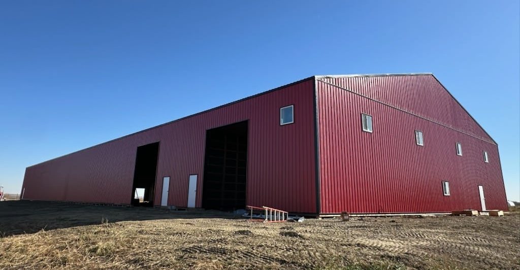 A bright red post-frame equestrian barn with overhead doors and a black roof