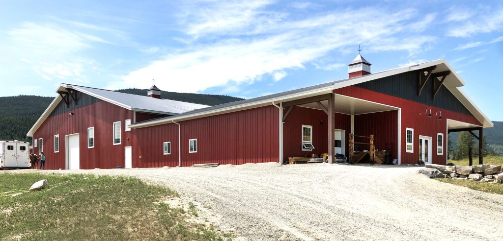 A tile red post-frame riding arena with overhead doors, timber accents, and soffits