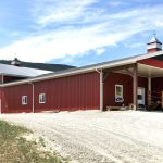 A tile red post-frame riding arena with overhead doors, timber accents, and soffits