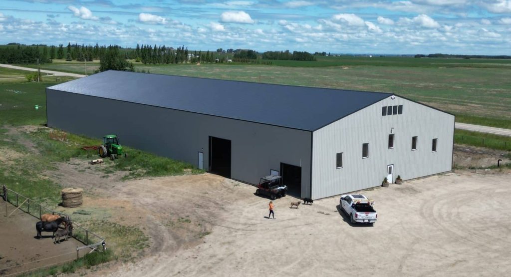 A stone grey post-frame riding arena with three overhead doors