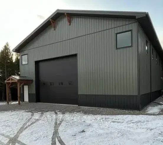 A dark sage post-frame shouse with open lean-tos, overhead doors, soffits, wainscoting, amd timber accents