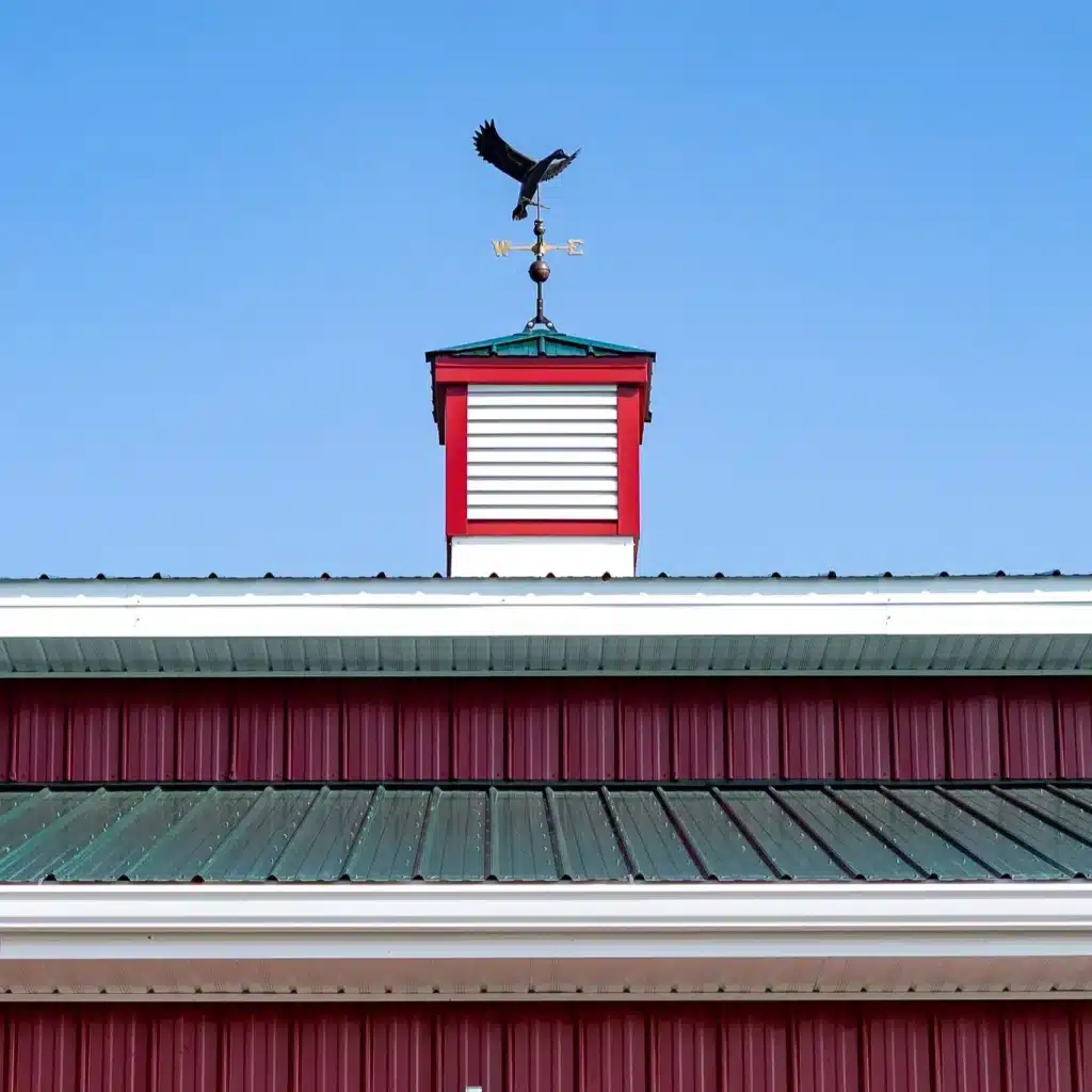 A dark red post-frame equestrian barn with a unique custom cupola
