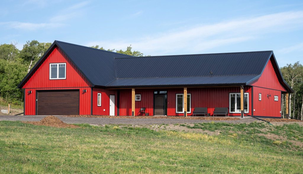 A dark red post-frame highwood with loft with an overhead door, front porch, and soffits