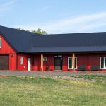 A dark red post-frame highwood with loft with an overhead door, front porch, and soffits