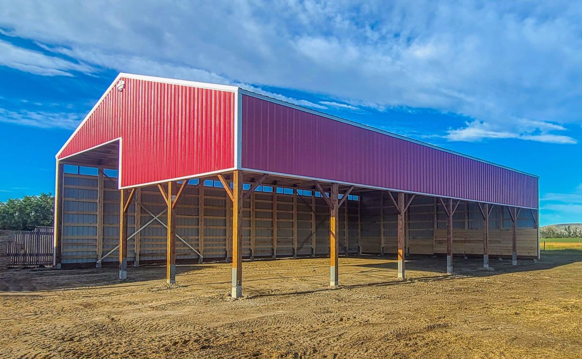 A dark red post-frame equestrian hay shed with a black roof