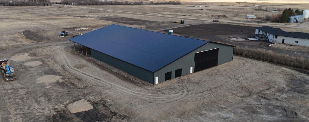 A gunmetal post-frame agricultural storage building with open and closed lean-tos, overhead and bi-fold doors