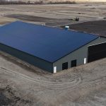 A gunmetal post-frame agricultural storage building with open and closed lean-tos, overhead and bi-fold doors