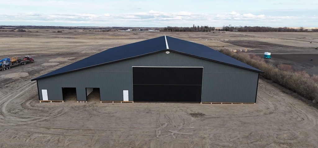A gunmetal post-frame agricultural storage building with open and closed lean-tos, overhead and bi-fold doors