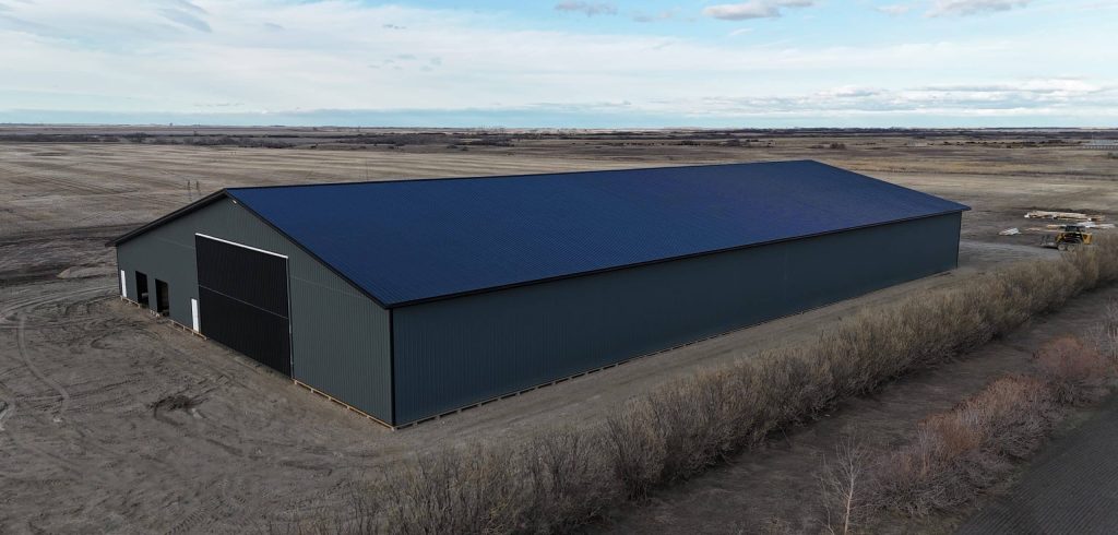 A gunmetal post-frame agricultural storage building with open and closed lean-tos, overhead and bi-fold doors