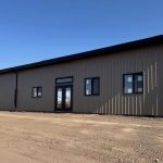 A buckskin post-frame Prairie Peak with soffits, closed lean-tos, and overhead doors