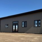 A buckskin post-frame Prairie Peak with soffits, closed lean-tos, and overhead doors
