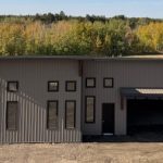 A buckskin post-frame Prairie Peak with soffits, closed lean-tos, and overhead doors