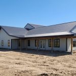 A white white post-frame custom residential build with soffits, open lean-to porch, and overhead doors