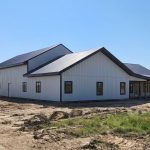 A white white post-frame custom residential build with soffits, open lean-to porch, and overhead doors