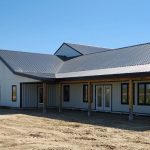 A white white post-frame custom residential build with soffits, open lean-to porch, and overhead doors