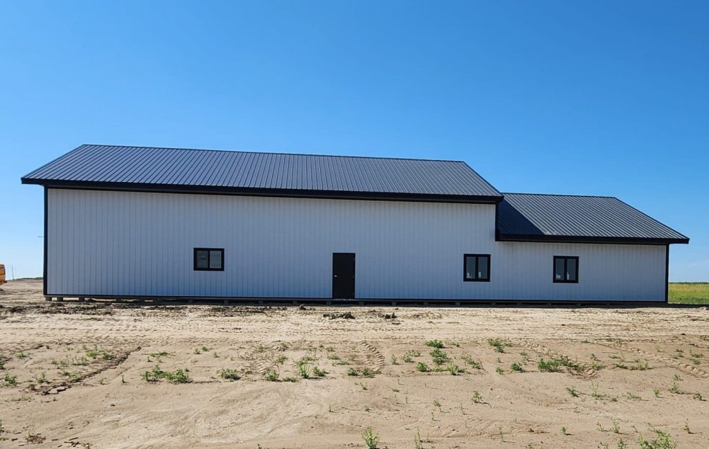 A white white post-frame custom residential build with soffits, open lean-to porch, and overhead doors