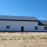 A white white post-frame custom residential build with soffits, open lean-to porch, and overhead doors