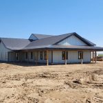 A white white post-frame custom residential build with soffits, open lean-to porch, and overhead doors
