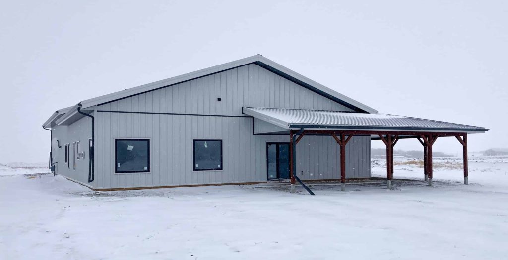 A white white post-frame Shouse with three overhead doors, two open lean-tos and soffits