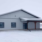 A white white post-frame Shouse with three overhead doors, two open lean-tos and soffits