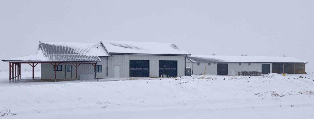 A white white post-frame Shouse with three overhead doors, two open lean-tos and soffits