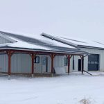 A white white post-frame Shouse with three overhead doors, two open lean-tos and soffits
