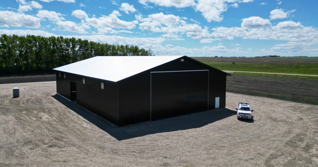 A black post-frame machine shed with a black bi-fold door and two overhead doors