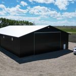 A black post-frame machine shed with a black bi-fold door and two overhead doors